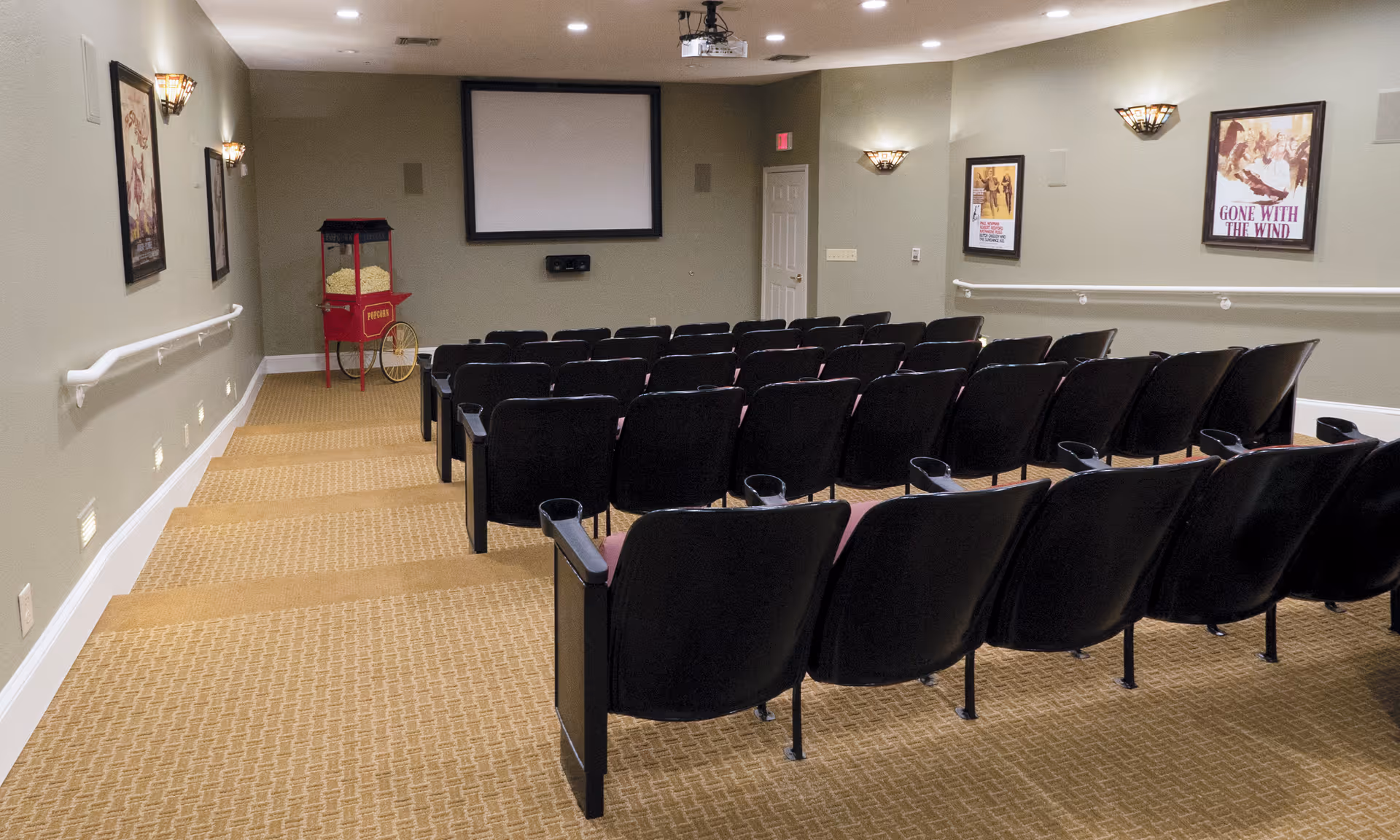 Small auditorium-style movie theater with rows of seats, a popcorn machine, and a projection screen.