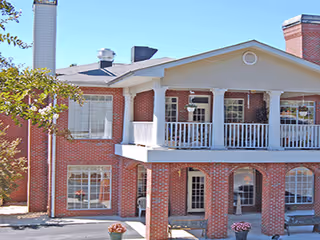 Front facade of a two-story red brick building with a covered upper balcony and arched lower porch.