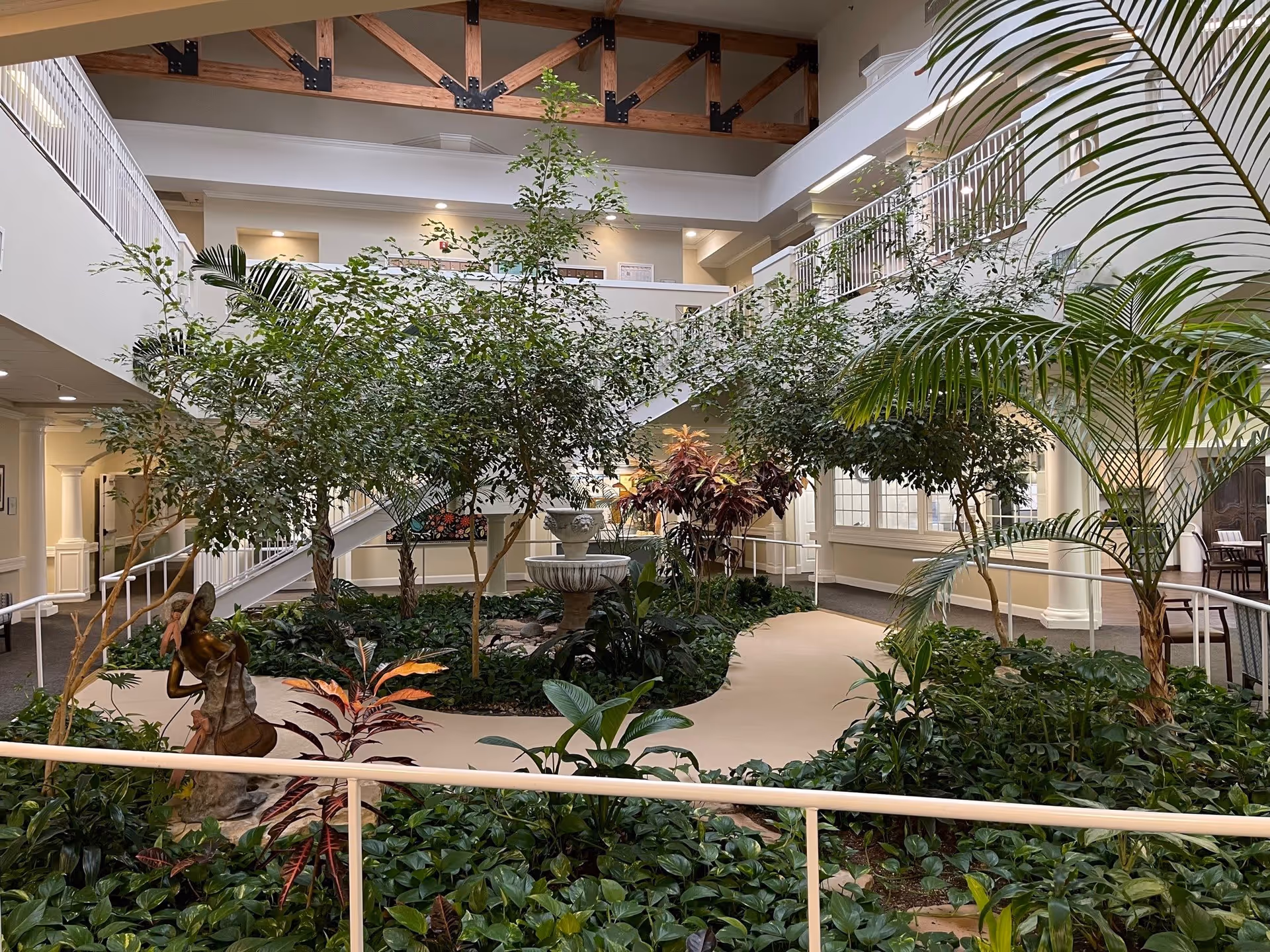 Indoor atrium with tropical plants, a central fountain, a sculpture, and surrounding walkways and balconies.