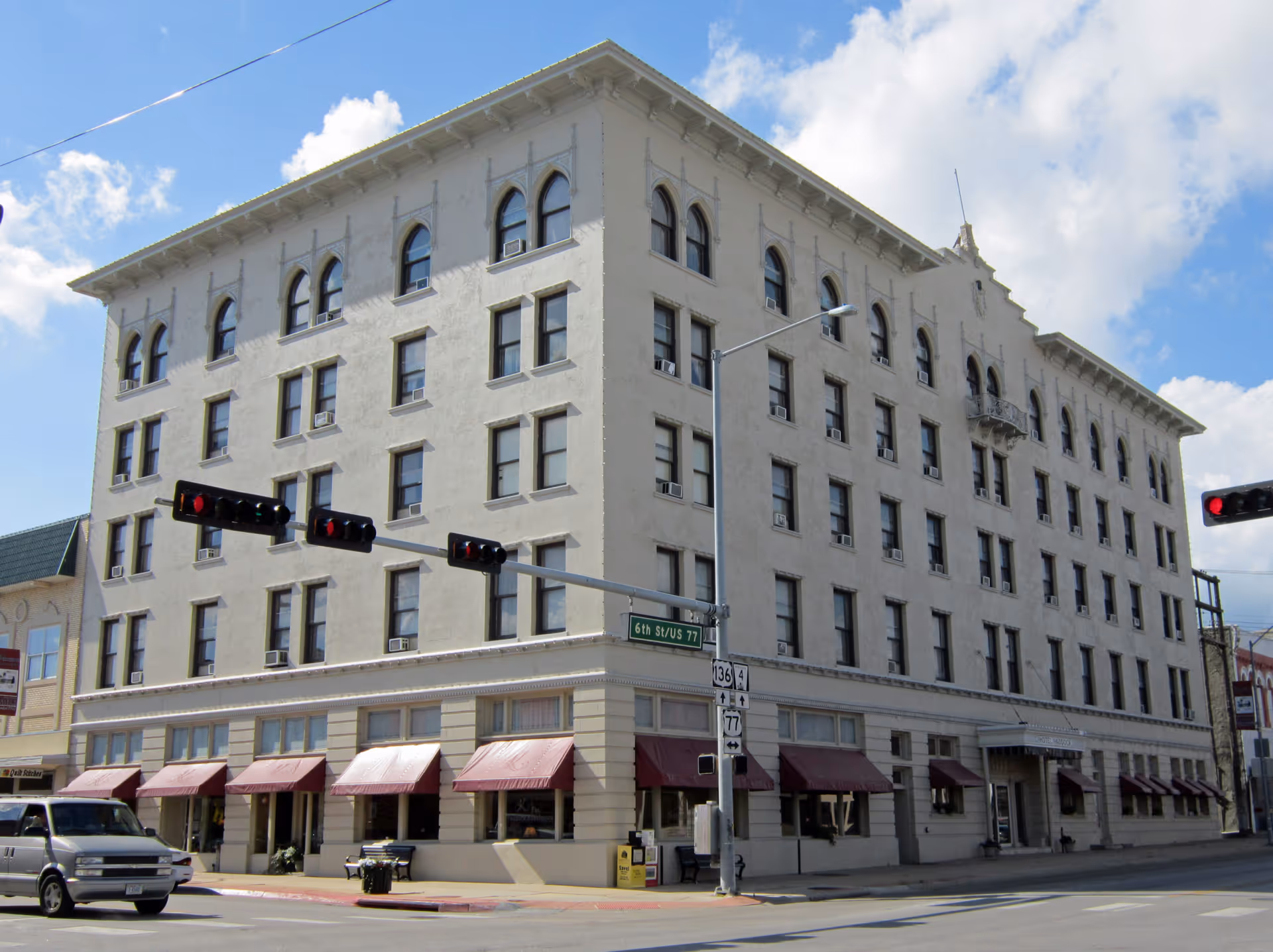 Six-story historic beige building with red awnings on a street corner and traffic lights in front.