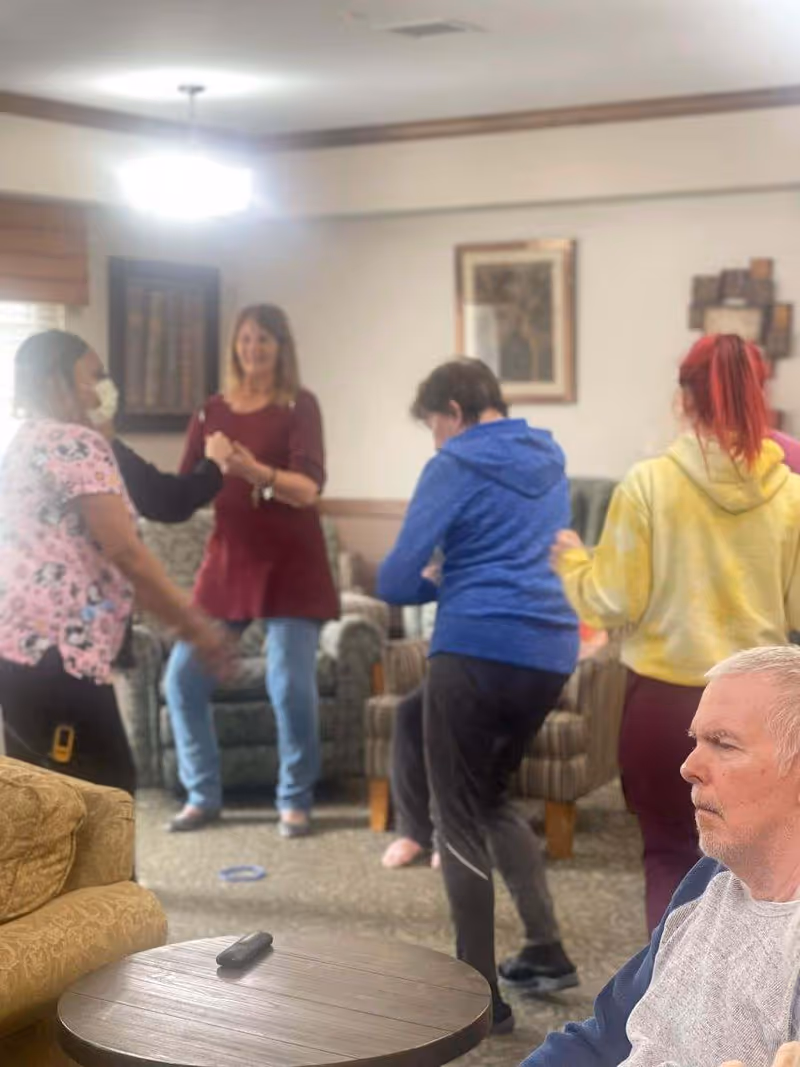 People dancing and socializing in a senior living facility's common living room.