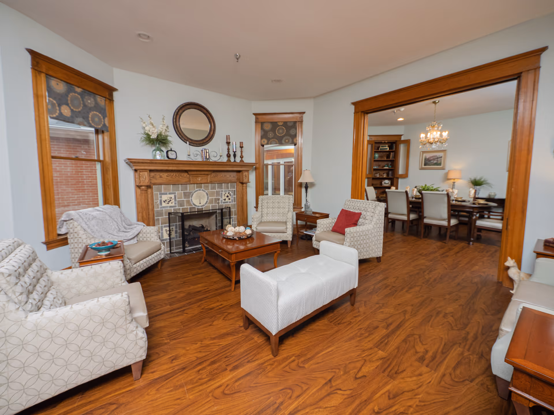 Cozy living room with armchairs and an ottoman arranged around a fireplace on hardwood floors, opening into a dining room.