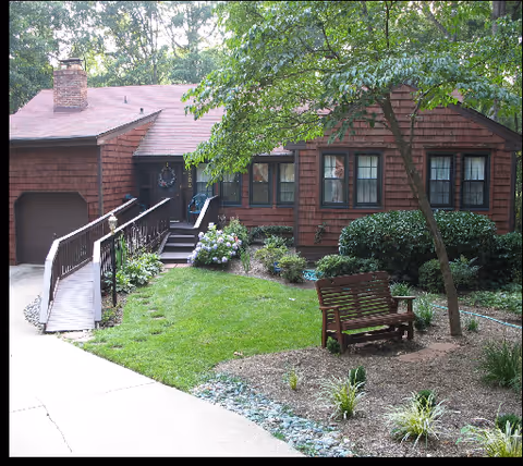 Front exterior of a brown wooden senior living facility with a ramp and garden.