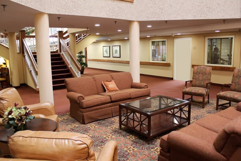 Spacious lounge area with sofas, armchairs, a glass-top coffee table on a patterned rug and a staircase in the background.