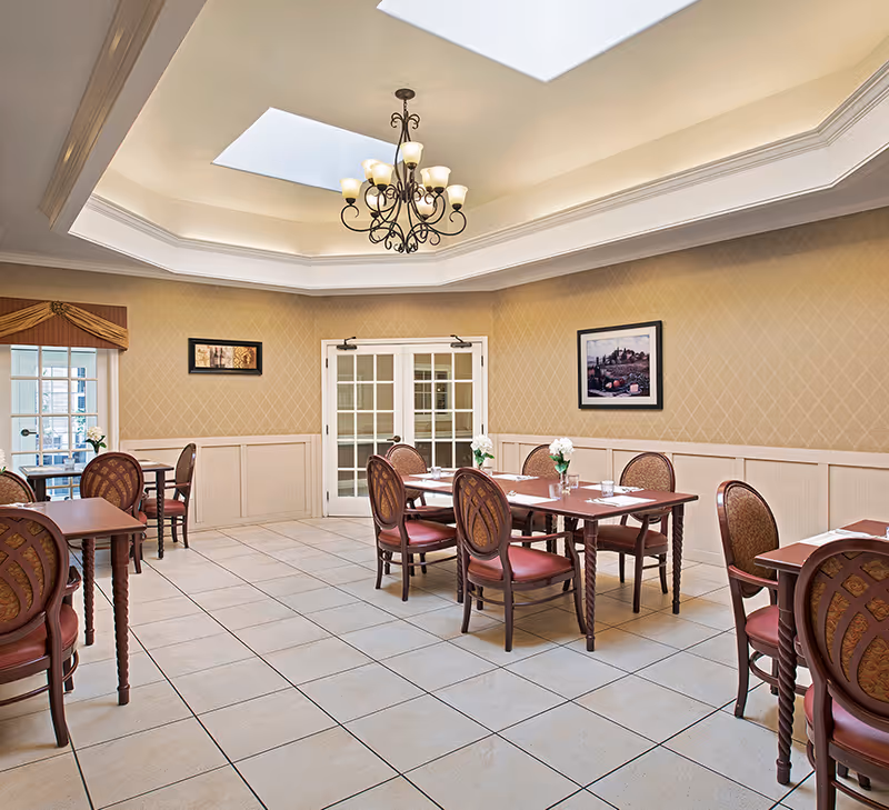 Dining room with multiple set tables and chairs under skylights and a central chandelier.