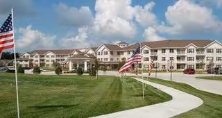 Front view of Parker Place Gracious Retirement Living with flags, curved walkway, and manicured lawn.