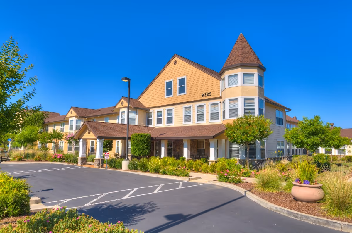 A beige, multi-wing senior living facility with a peaked front and clear blue sky.