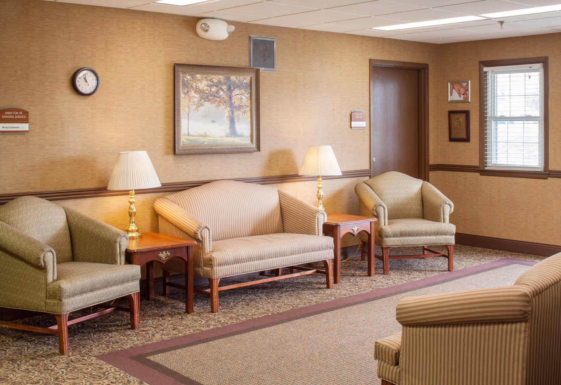 A quiet sitting area with upholstered sofas and armchairs, wooden side tables, lamps, wall art, and a window.