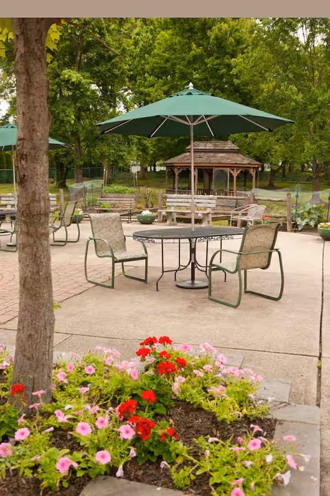 Outdoor courtyard with tables, chairs, umbrellas, a gazebo, and colorful flowers.