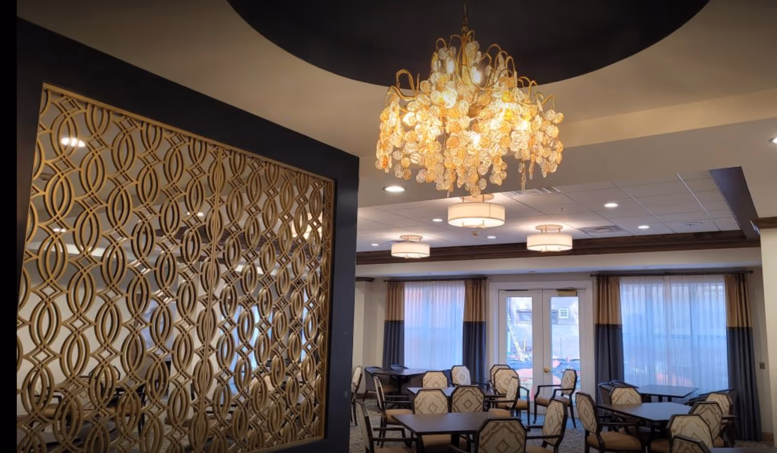 Well-lit dining/lounge area with multiple tables and chairs, a decorative gold partition, and a central chandelier.