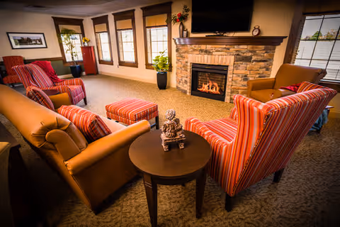 Cozy living room with striped armchairs and a leather sofa arranged around a stone fireplace and wall-mounted TV.