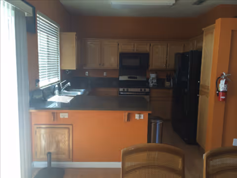 Open kitchen with orange walls, wood cabinets, black appliances, and a breakfast bar.