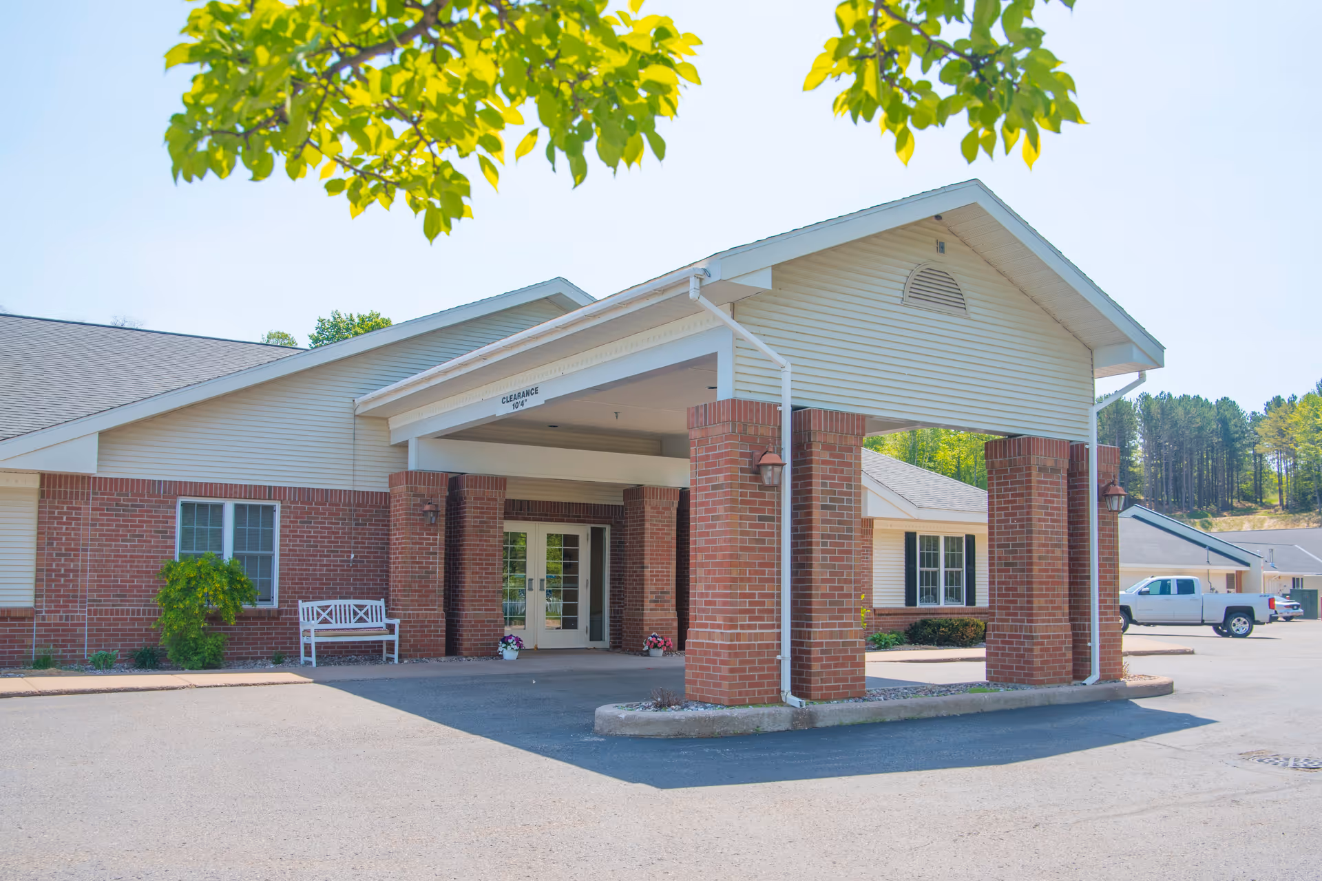 Covered front entrance of a brick-and-siding senior living facility with a porte-cochère and a parked truck.