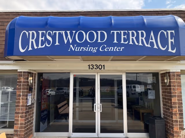 Entrance of Crestwood Terrace Nursing Center with a blue awning displaying the facility name above glass double doors and the street number 13301 above the doors.