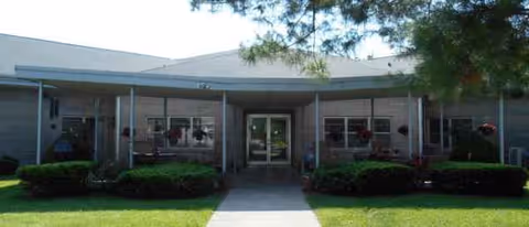 Front view of a single-story senior living facility entrance with manicured shrubs.