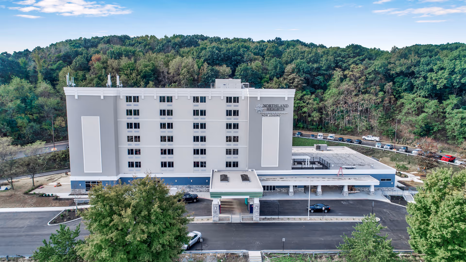 Exterior front view of a multi-story assisted living and memory care facility named Northland Heights, surrounded by trees and greenery with a parking area in front.