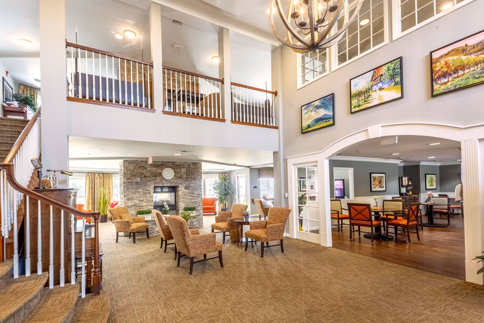 Spacious two-story communal lounge with armchairs around a fireplace and an adjacent dining area.