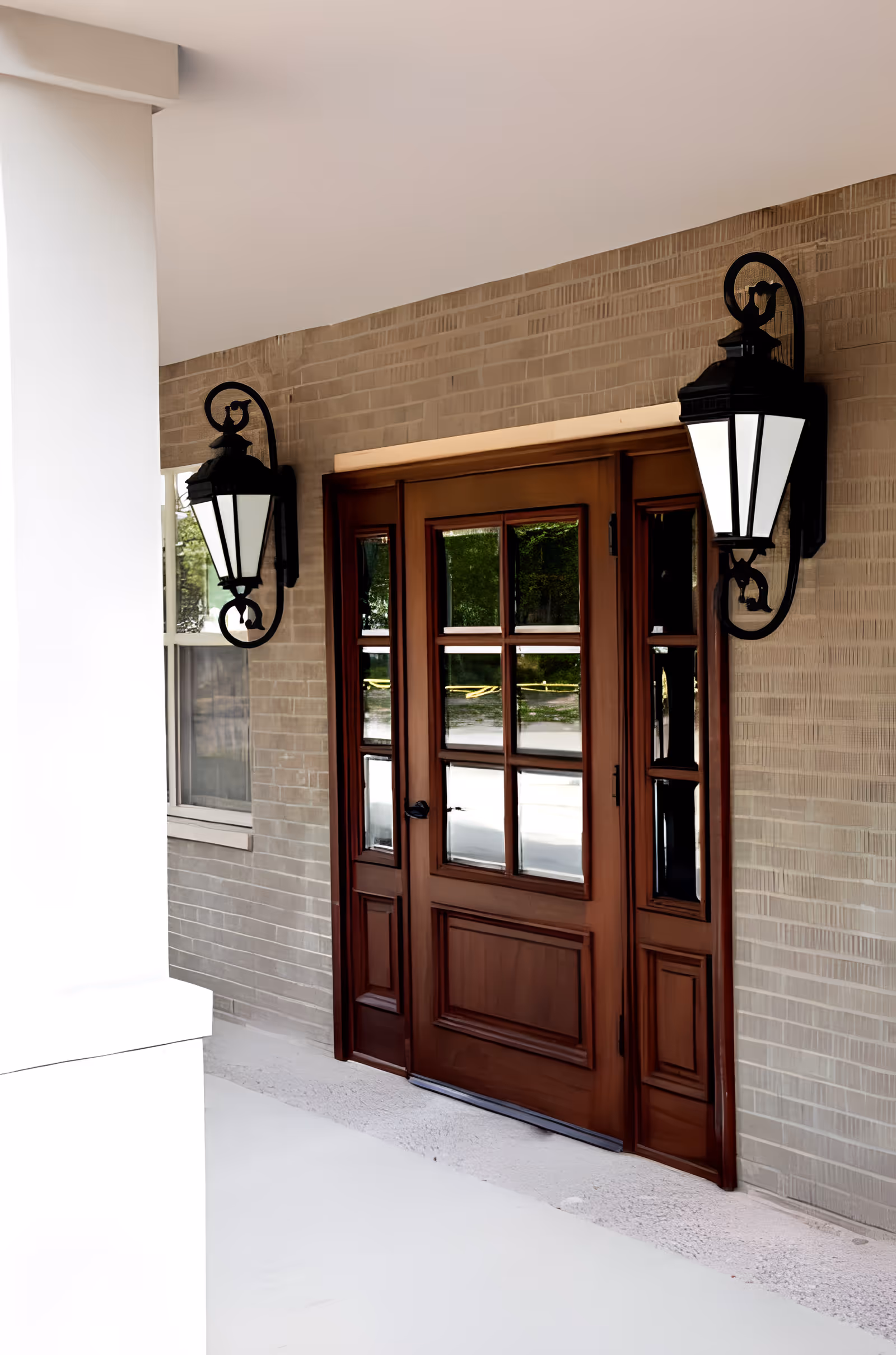 Wooden front door with glass panels on a brick wall, flanked by two black outdoor lantern-style wall lights.