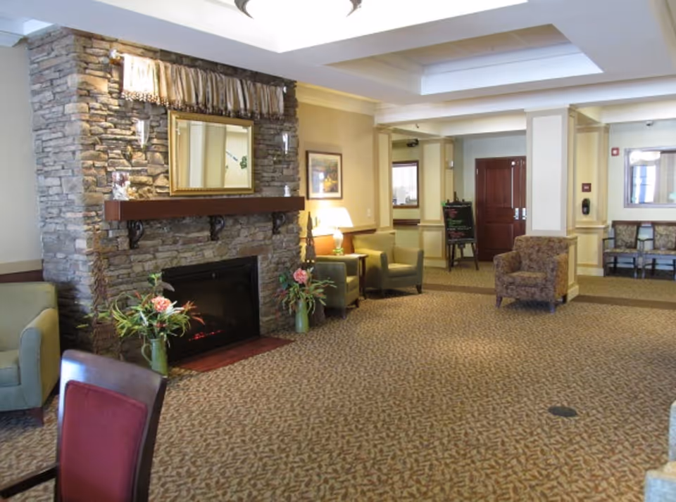 Spacious assisted-living lobby with a stone fireplace, multiple seating areas, and decorative plants.