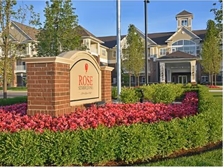 Exterior view of Rose Senior Living Providence Park with a brick sign and landscaped entrance