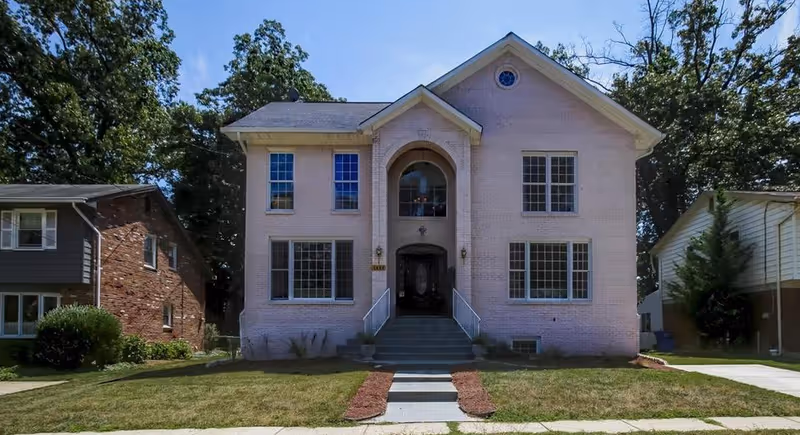 A two-story pale brick senior living facility with a central arched entrance.