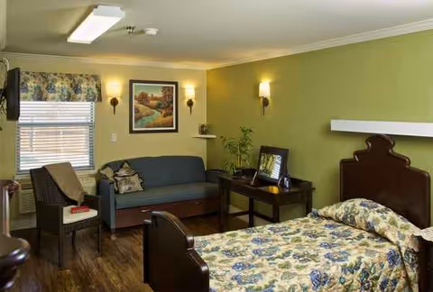 Bedroom suite in a senior living space with bed, seating area, and green walls.