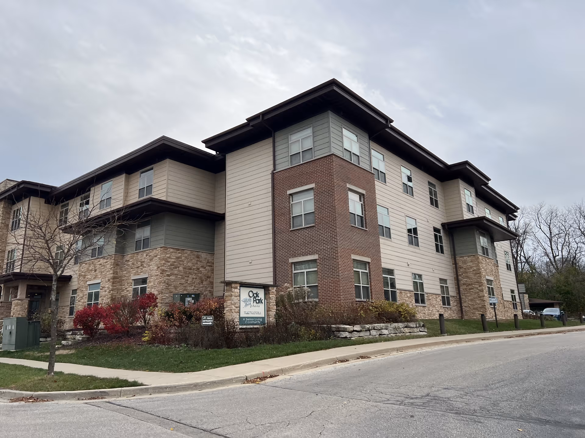 Three-story senior residence with brick, stone, and siding facade and landscaped front viewed from the street.