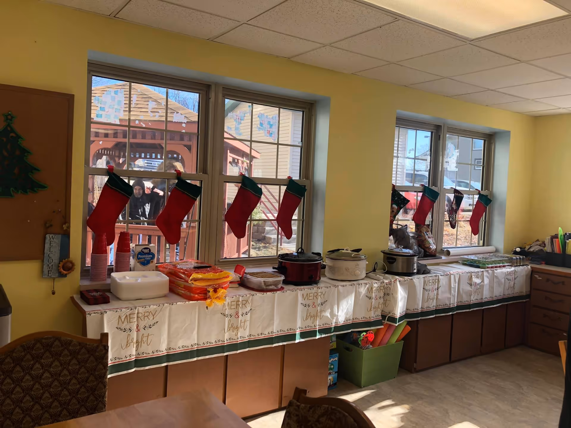 A holiday-decorated serving counter with crockpots, snacks and stockings hung on the windows in a communal dining area.