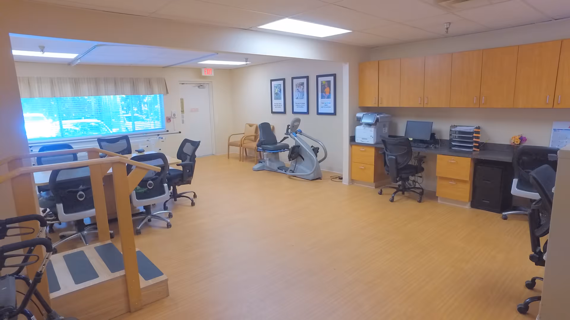 A bright multipurpose activity room with desks, office chairs, an exercise bike and workstations.