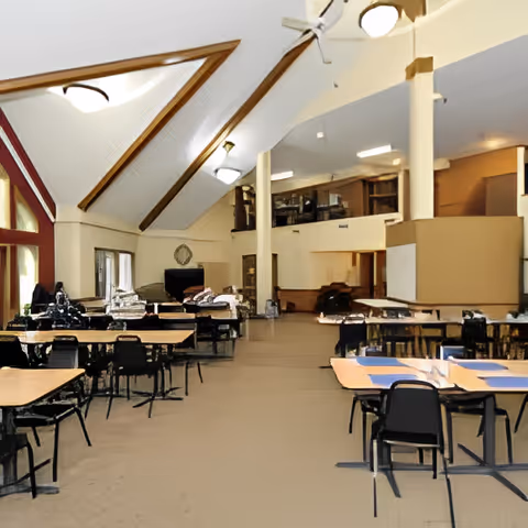 Large dining hall with multiple tables and chairs under a vaulted ceiling with exposed beams.