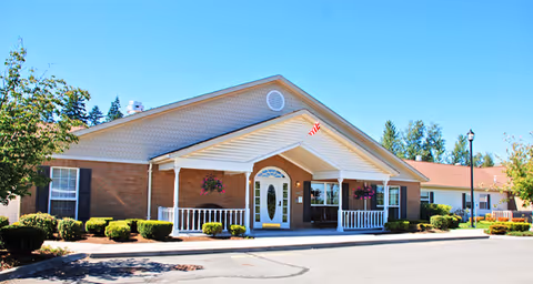 Front exterior view of a single-story brick building with a covered entrance, white railings, hanging flower baskets, and a clear blue sky above.