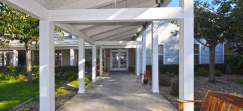 Covered walkway with white columns leads to the entrance of a light-blue senior living building.