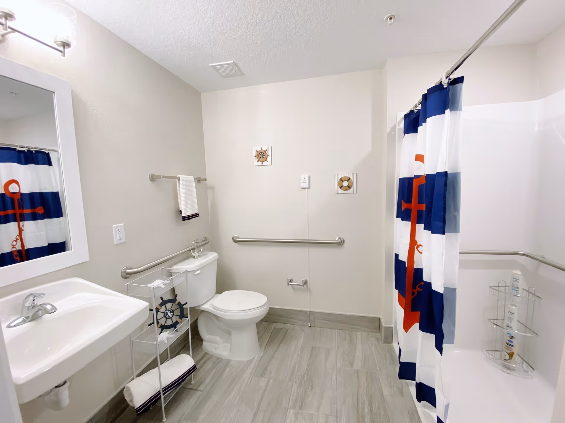 Bright accessible bathroom with a sink, toilet, grab bars, and a nautical-themed shower curtain.