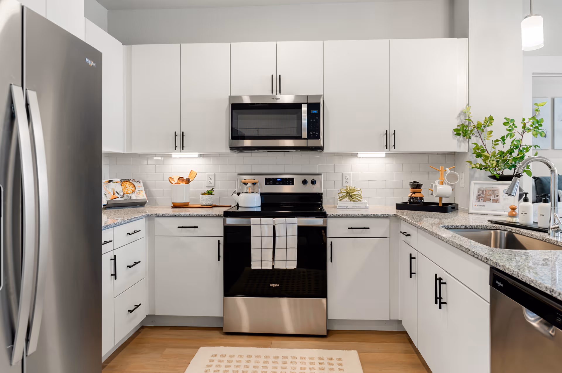 Bright modern kitchen with white cabinets, stainless steel refrigerator, oven and microwave, granite countertops and a sink.