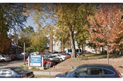 Parking lot area with several parked cars surrounded by trees with autumn foliage. A sign near the entrance reads Burlington Health & Rehab. A multi-story building is visible in the background.