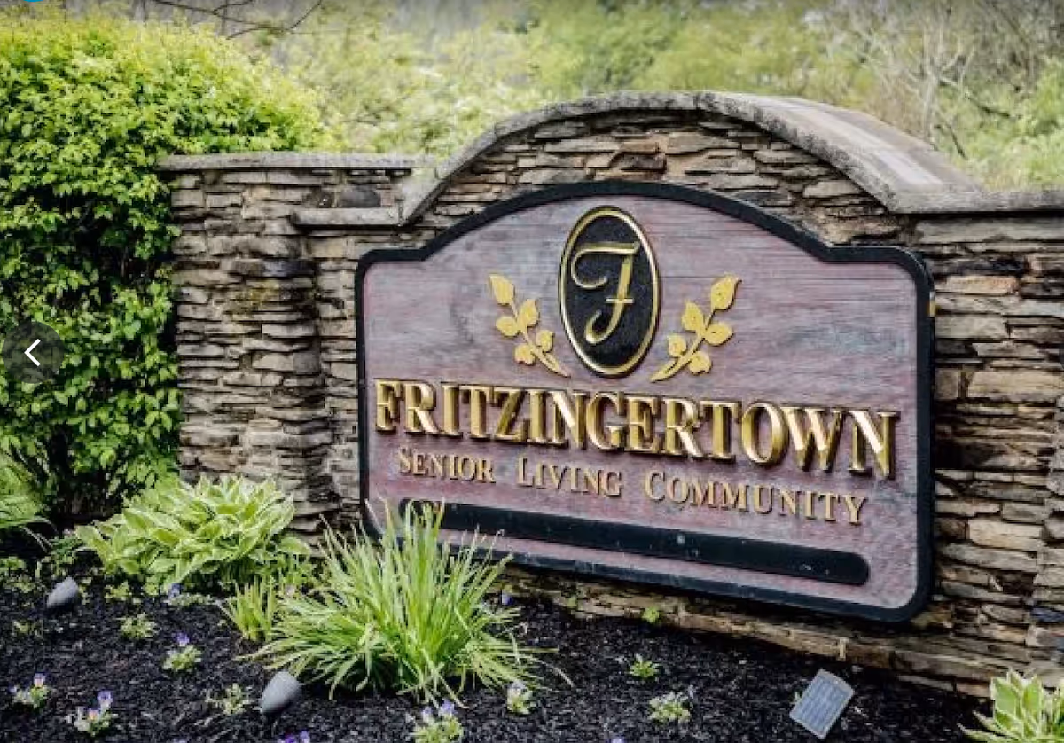 A stone and wood sign for Fritzingtown Senior Living Community surrounded by green plants and landscaping.