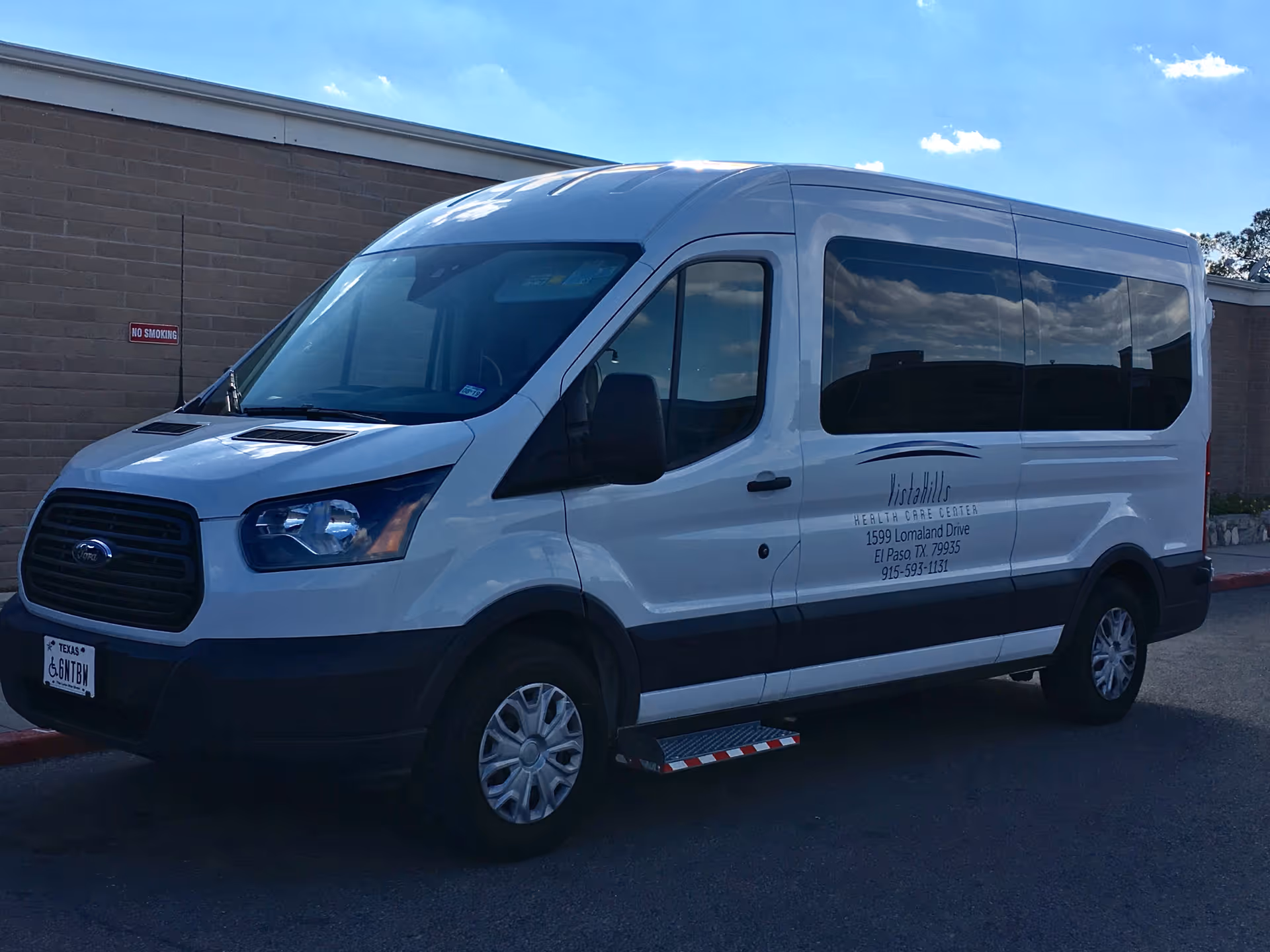 A white Vista Hills Health Care Center passenger van parked outside a brick building under a blue sky.