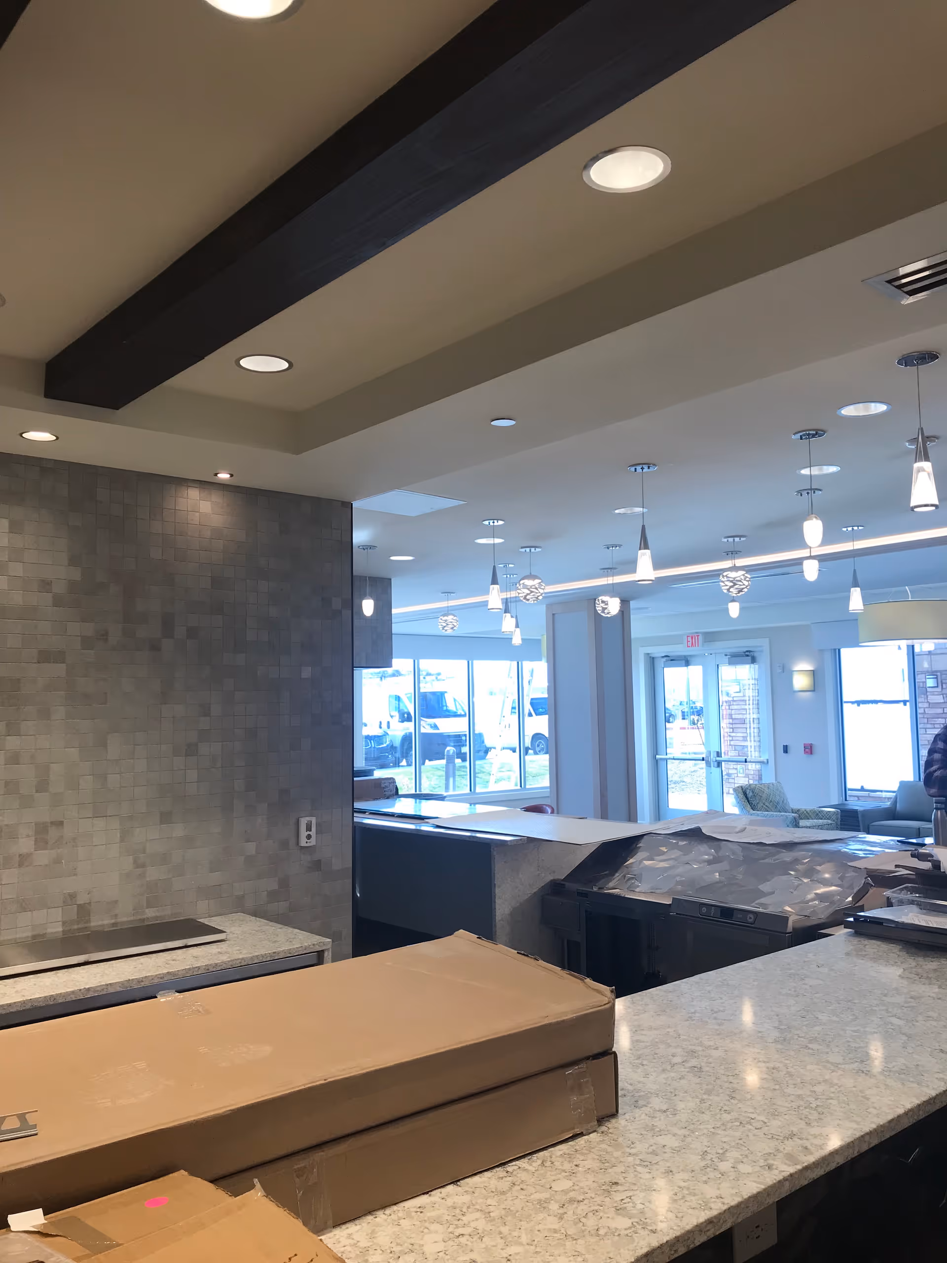 Interior view of a senior living facility common area with marble countertops, boxed packages on the counter, pendant lights, and large windows by the entrance.