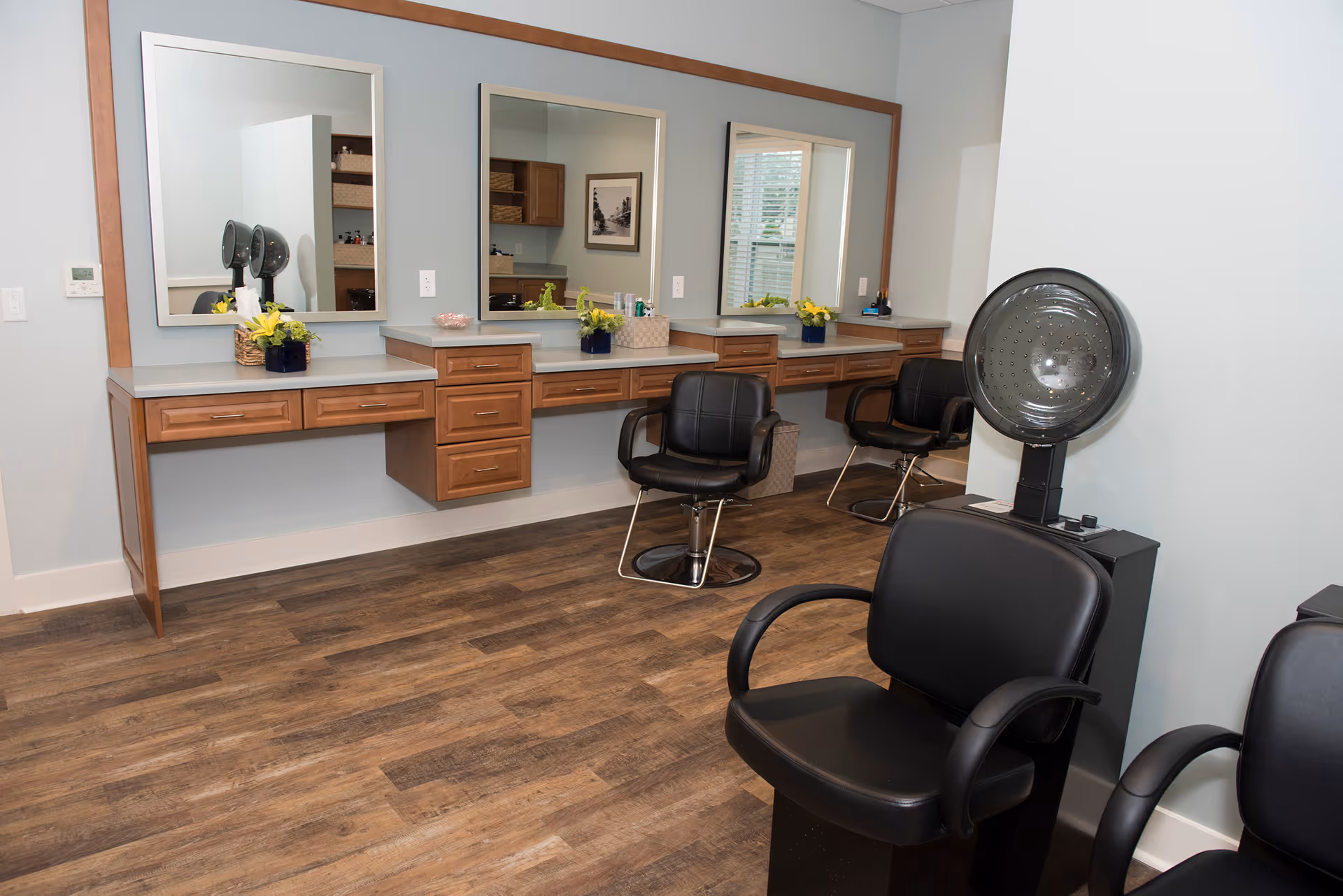 Interior salon with styling chairs, mirrors, wooden counters and a hooded hair dryer.
