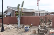 Single-story building behind a low stucco wall with a gated entrance, desert landscaping, potted plants, and an American flag.