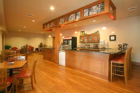 Warm wood-floored dining area with a countertop cafe/bar, tables and chairs, and pendant lights.