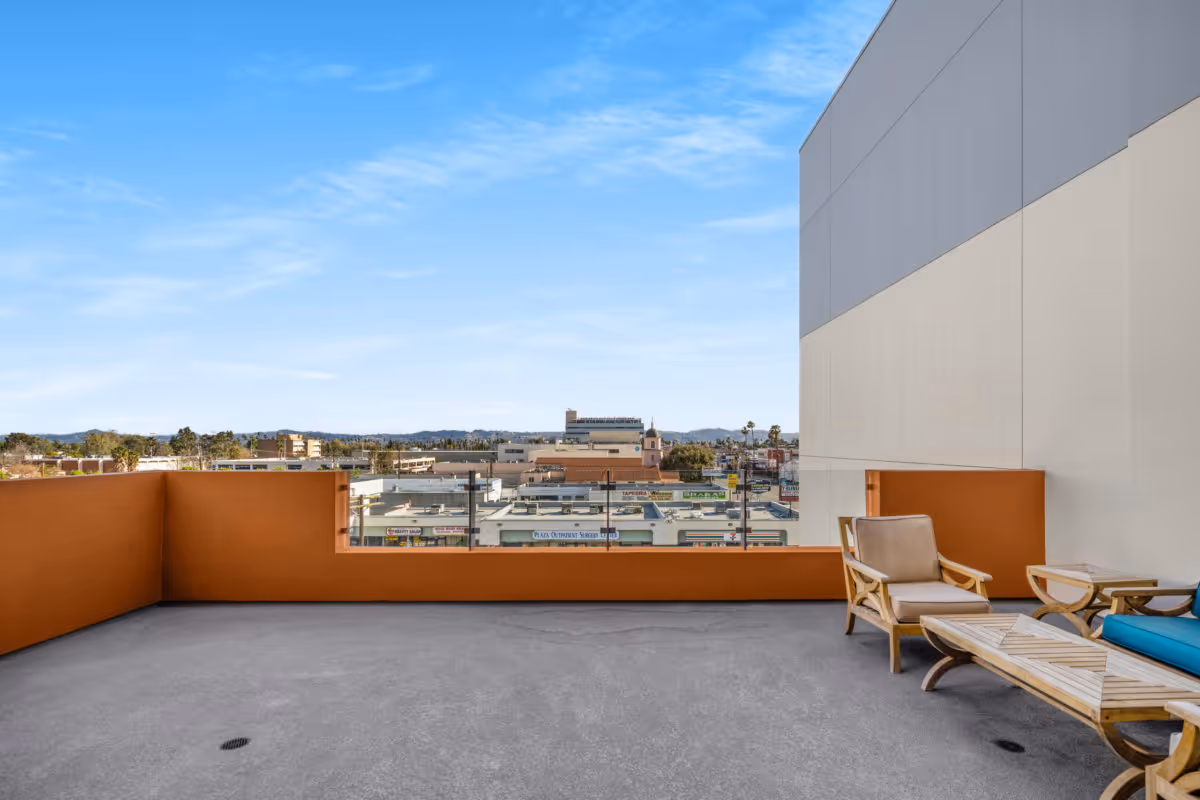 A rooftop terrace with lounge chairs, a low orange parapet and a view over the city skyline.