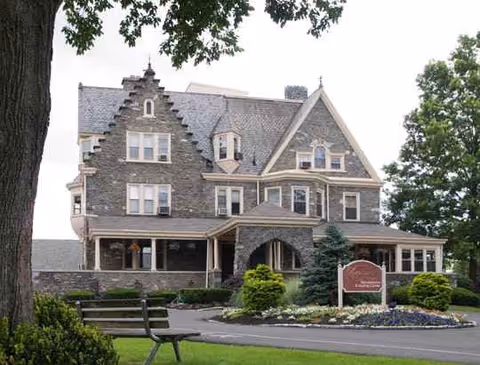 Stone-front senior living facility with arched entry, sign, and landscaped front lawn.