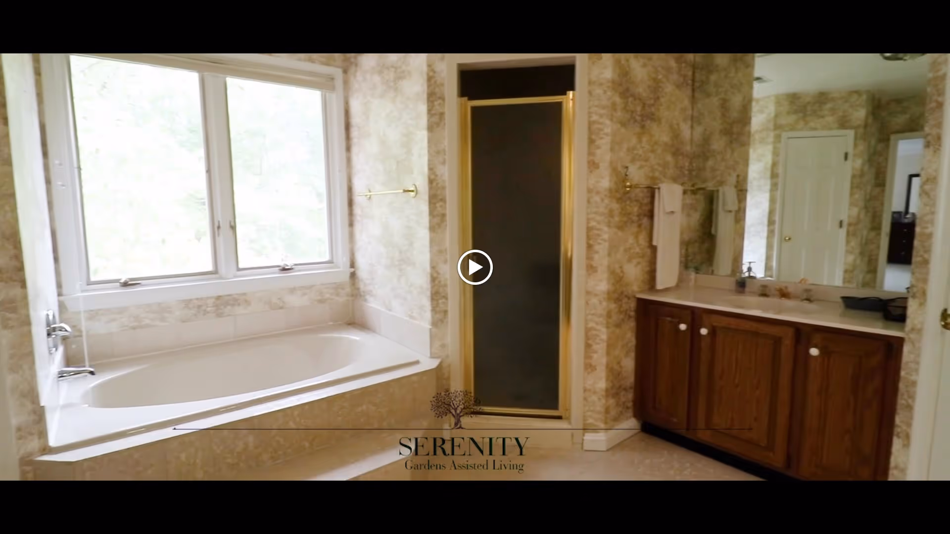 A bathroom with a large bathtub under a window, a separate shower with a glass door, and a wooden vanity with a sink and mirror. The walls have a textured wallpaper and there are towel racks with white towels.