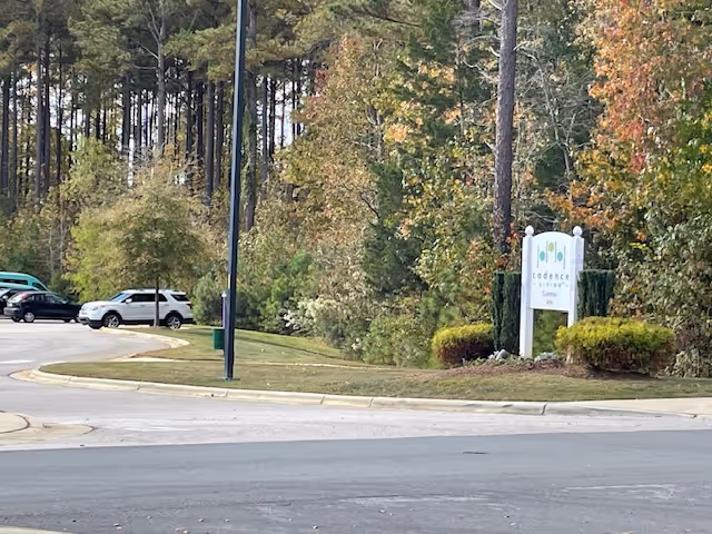 Entrance drive and parking area beside trees with a white sign reading Cadence Garner.