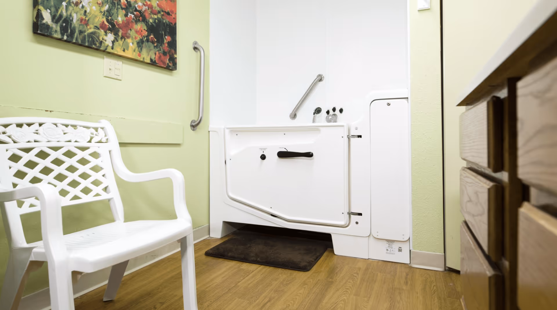 Accessible bathroom featuring a white walk-in tub with grab bars, a white plastic chair, and wood cabinetry.