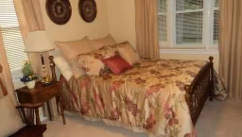 A floral quilted bed with a nightstand sits in a cozy senior care home bedroom.
