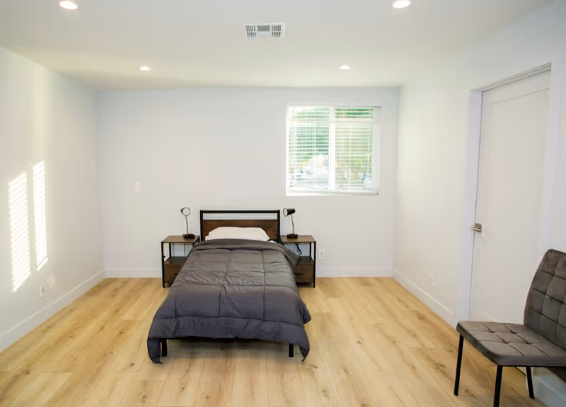 A minimalist bedroom with a single bed, two nightstands, a window, and a chair