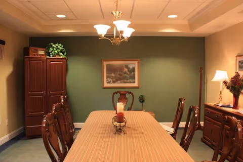 Formal dining room with a long striped table, wooden chairs, chandelier, green accent wall, and sideboard.