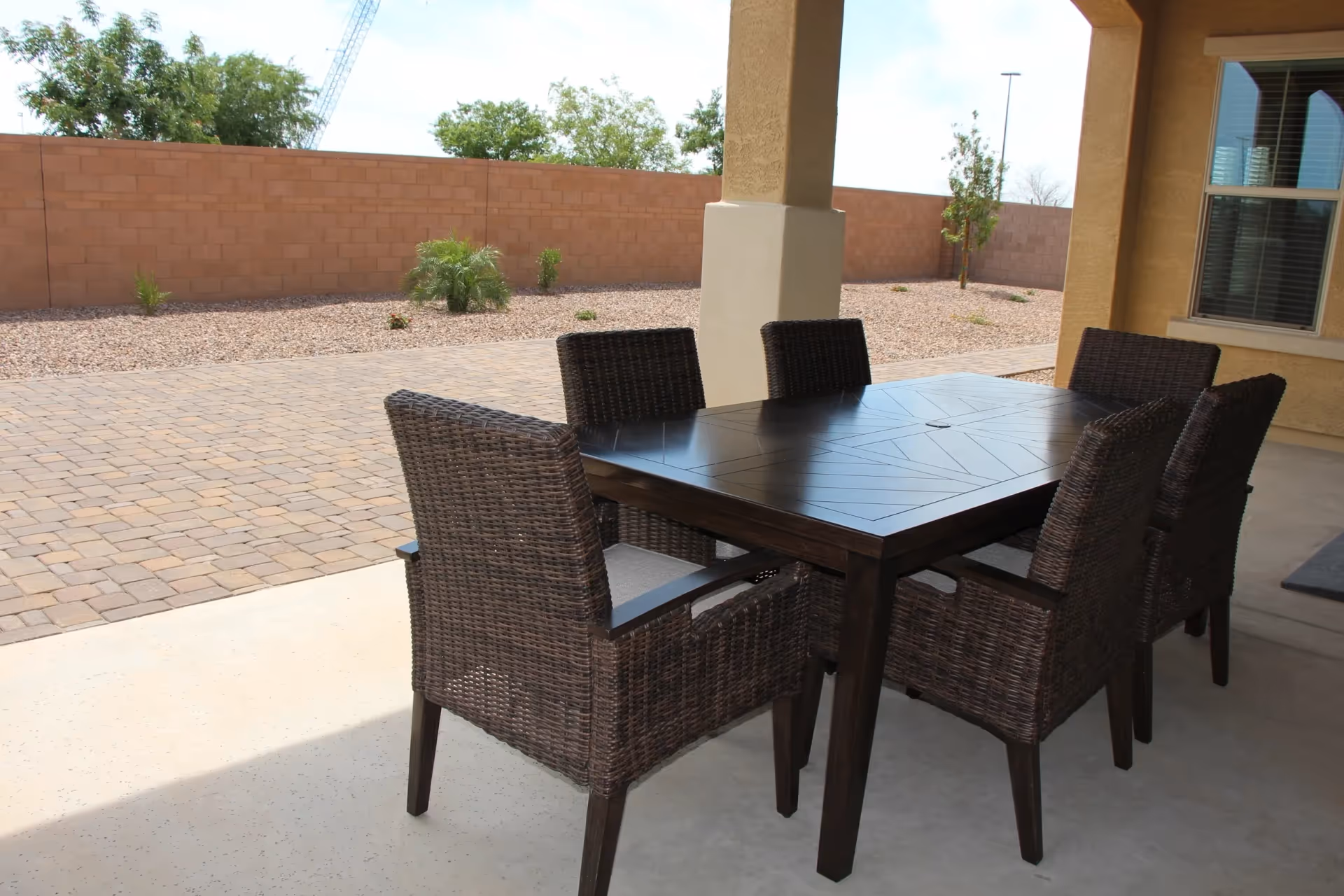 Outdoor patio with a dark wicker dining table and six chairs under a covered porch.
